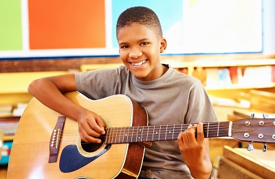 child with a smile holding a
            guitar